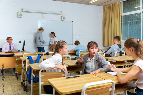 Group of smiling teen pupils chatting in break between lessons indoors