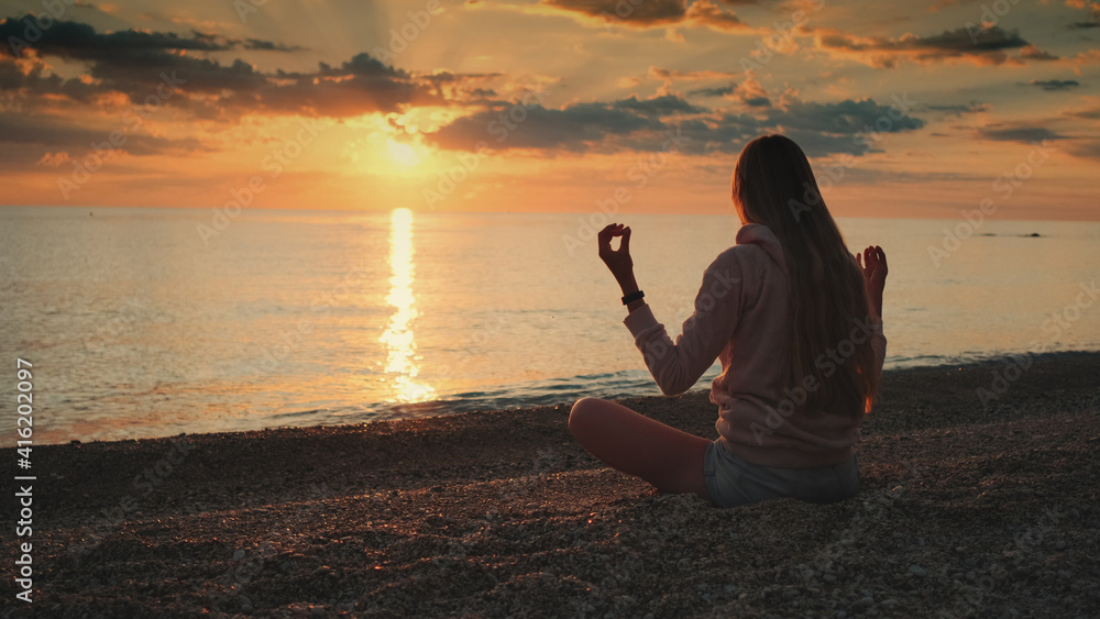 Medium long shot of woman having meditation over the sea before sunset. Silence and relaxation concept.