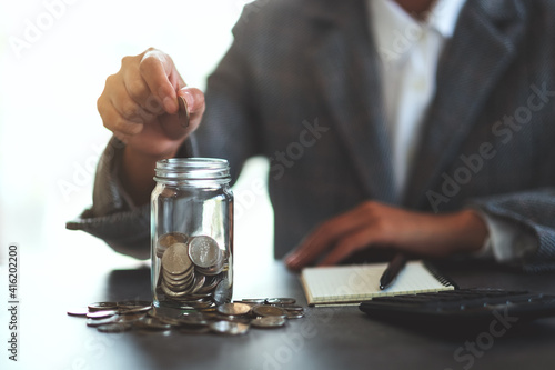 Closeup image of a businesswoman collecting and putting coins in a glass jar for saving money concept