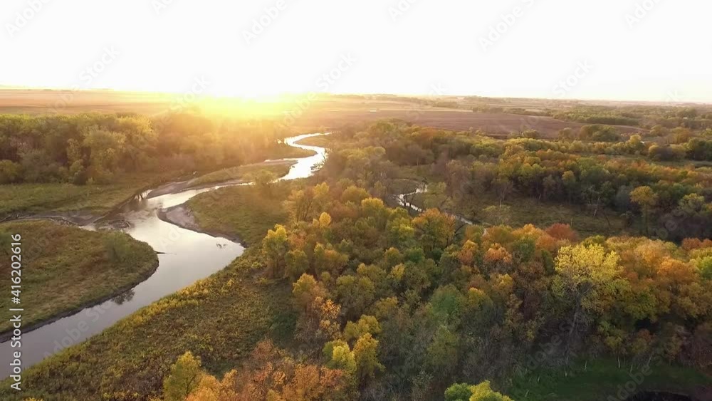 Drone shot over creek surrounded by fall colored trees during sunset Drone shot over creek surrounded by fall colored trees during sunset