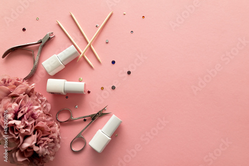 A set of manicure tools and accessories on a pink background with flowers and rhinestones. Nail care. Flat lay. Copy space. Women's Day. March 8