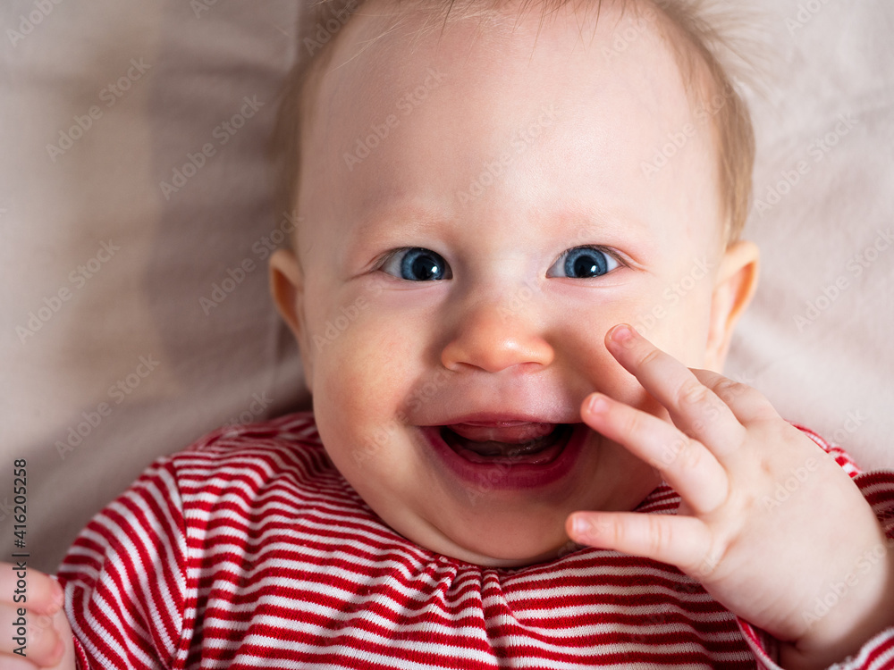 Portrait of a baby girl, 8 months old, looking at the camera, laughing, top view, close-up. A mischievous, beautiful girl with fair skin and hair, with big blue eyes. Funny facial expression Portrait of a baby girl, 8 months old, looking at the camera, laughing, top view, close-up. A mischievous, beautiful girl with fair skin and hair, with big blue eyes. Funny facial expression
