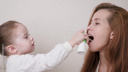 A little daughter heals her mother's cold and throat by spraying medicine into her mouth. Mom plays with child who is sick with flu. The child provides medical care to his sick mother. Healthy family