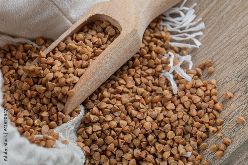 Obraz premium A wooden spoon full of raw buckwheat on a wooden table