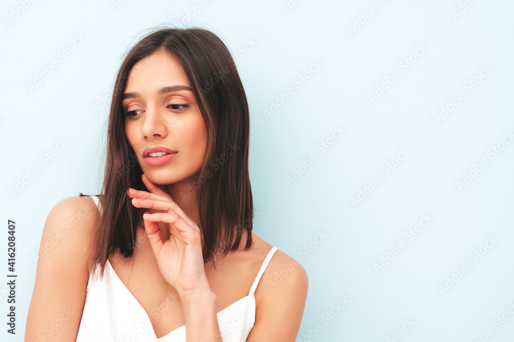 Portrait of beautiful smiling woman dressed in white pajamas. Sexy carefree cheerful model enjoying her morning. Adorable and positive female posing near light blue wall in studio. Tanned and skinny Portrait of beautiful smiling woman dressed in white pajamas. Sexy carefree cheerful model enjoying her morning. Adorable and positive female posing near light blue wall in studio. Tanned and skinny