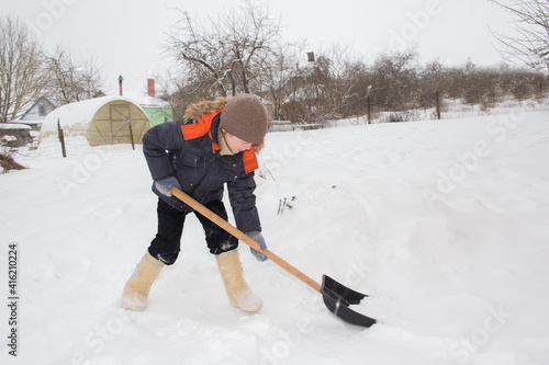 The boy cleans the snow with a shovel. It is snowing, small snowflakes all over the frame.