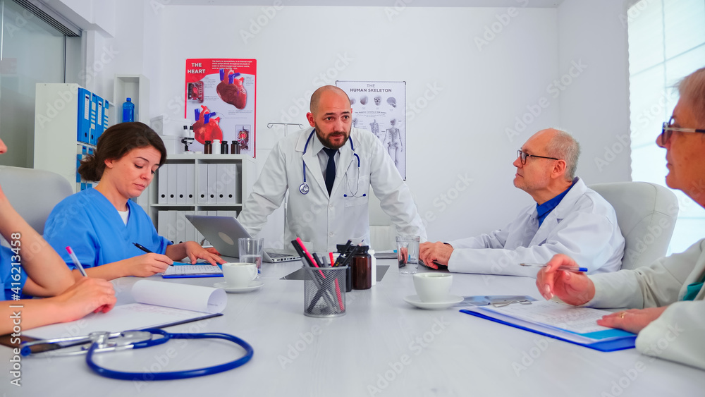 Young medical specialist discussing about patient diagnosis with coworkers in hospital conference room. Clinic expert therapist talking with colleagues about disease, medicine professional Young medical specialist discussing about patient diagnosis with coworkers in hospital conference room. Clinic expert therapist talking with colleagues about disease, medicine professional