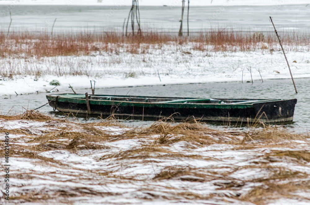 Fototapeta premium Forgotten wooden fishing boats in the frozen water of the Danube tributary, covered with snow. Vojvodina, Novi Sad, Serbia.