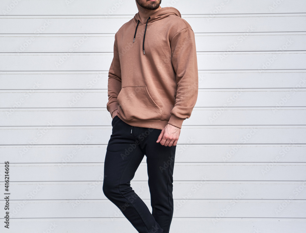 Man is standing in brown hoodie and dark pants. Man is wearing light suede  stylish long sleeve sweater. Stock Photo | Adobe Stock