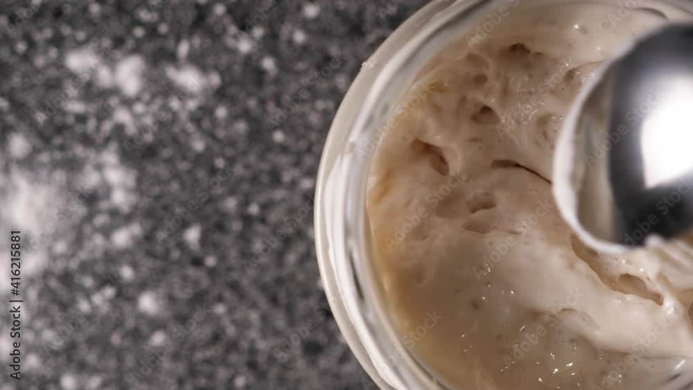 Close-up top view of a spoon stirring sourdough wheat leaven in a jar on a table with copy space. High quality FullHD footage Close-up top view of a spoon stirring sourdough wheat leaven in a jar on a table with copy space. High quality FullHD footage