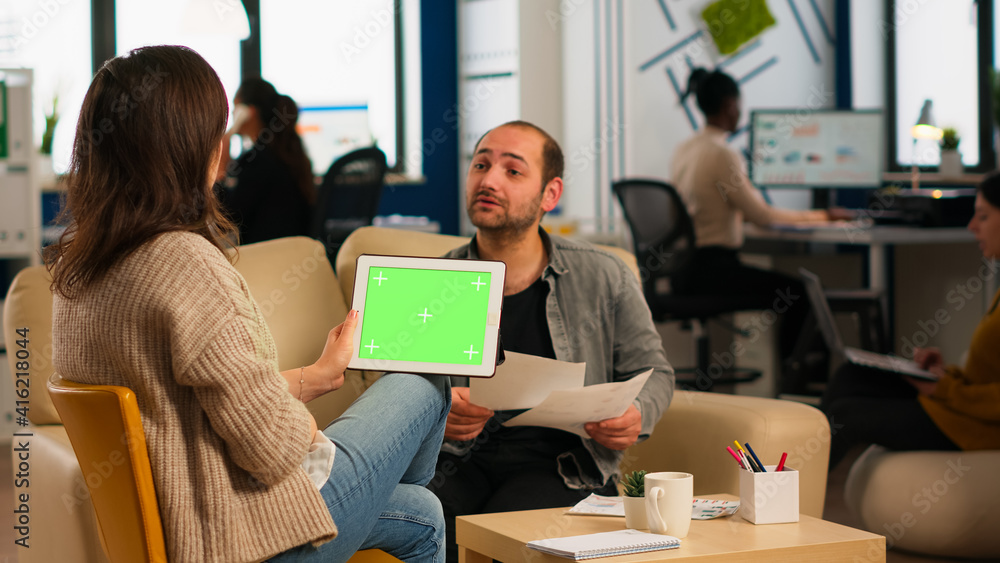 Back view of businesswoman sitting on couch using tablet with green screen talking with colleague while team working on background. Multiethnic coworkers planning project on chroma key display Back view of businesswoman sitting on couch using tablet with green screen talking with colleague while team working on background. Multiethnic coworkers planning project on chroma key display