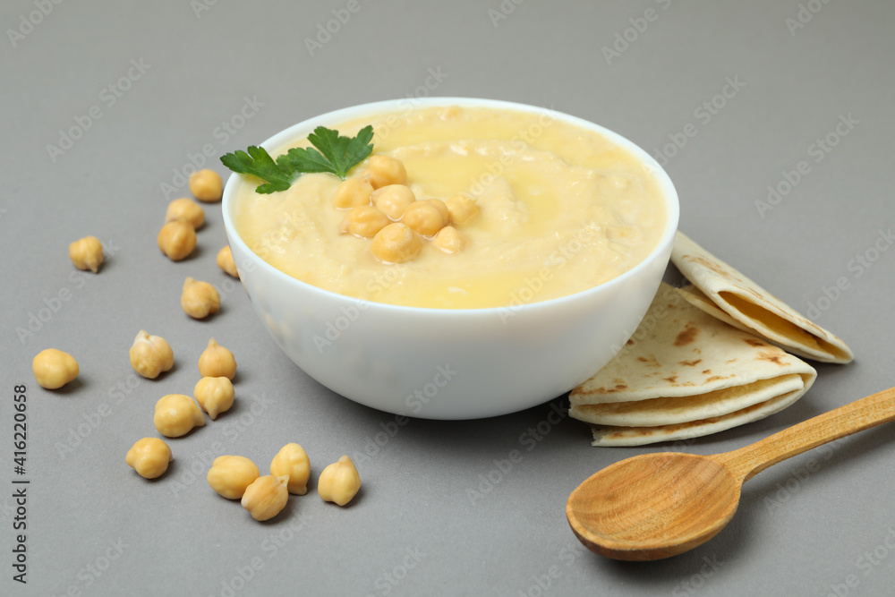 Bowl of hummus, pita and spoon on gray background