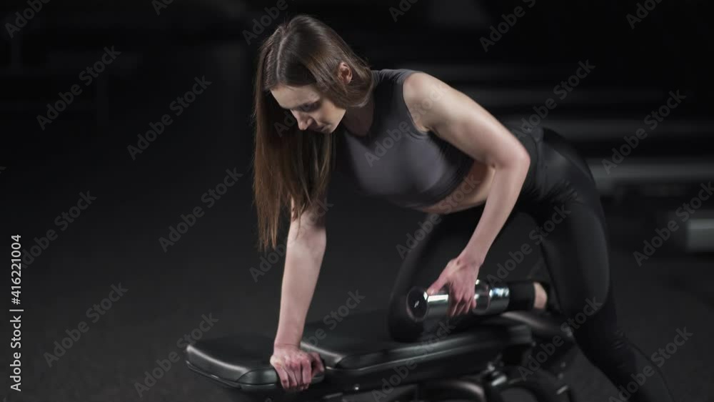 Young female in the gym, woman lifts a dumbbell in a tilt, muscle training with weights. Young female in the gym, woman lifts a dumbbell in a tilt, muscle training with weights.