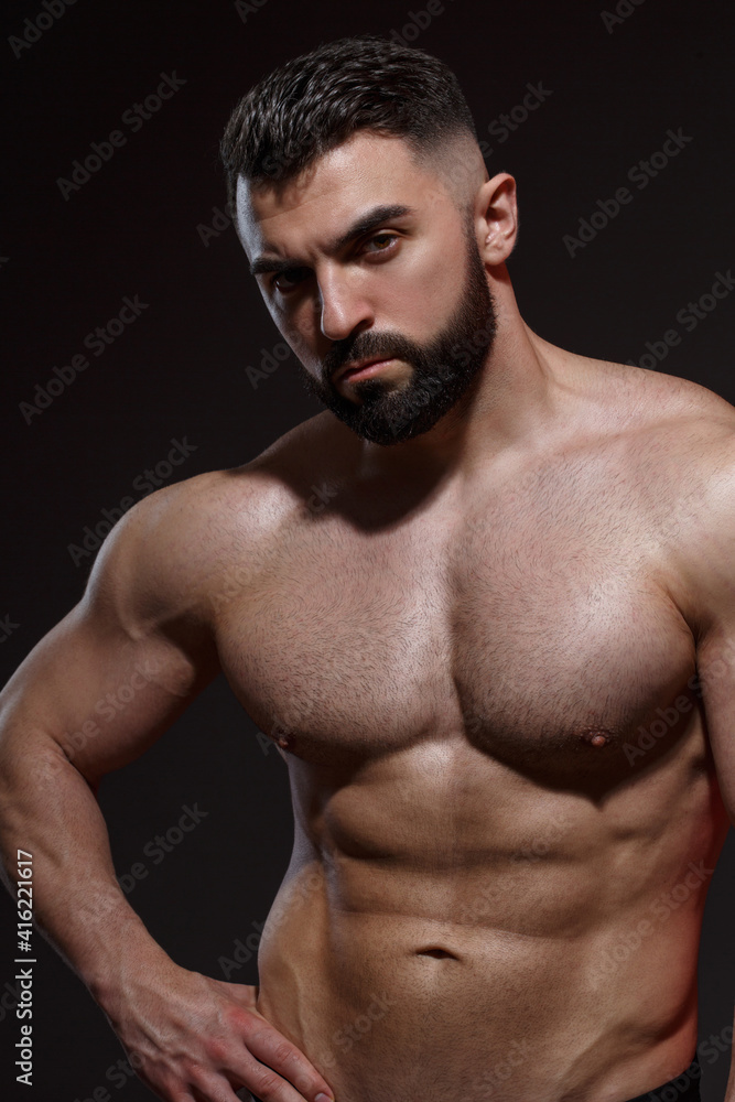 Young athletic male athlete with a beard shows muscles isolated on a dark background.