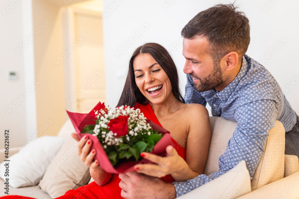 Excited young woman receiving unexpected Bouquet of red roses from husband at home, loving generous boyfriend making romantic surprise to attractive girlfriend on Valentines day occasion Excited young woman receiving unexpected Bouquet of red roses from husband at home, loving generous boyfriend making romantic surprise to attractive girlfriend on Valentines day occasion