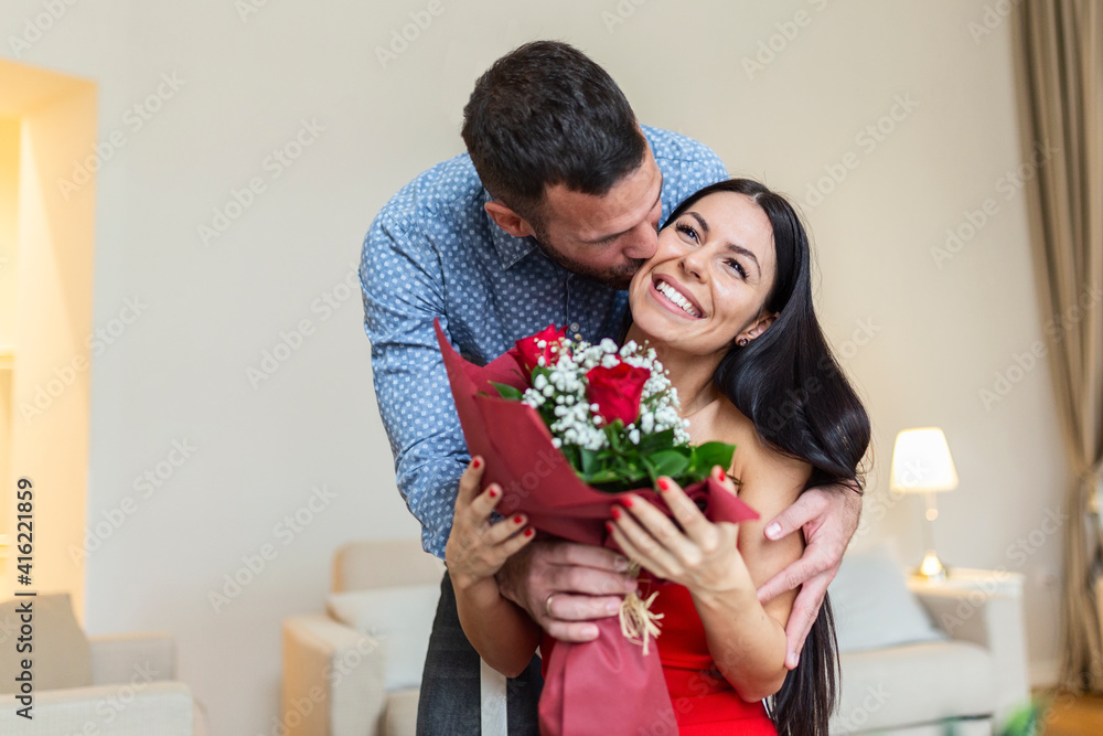 Beautiful, happy, positive couple kissing, holding bouquet of red roses, 8 March happy women's day. Handsome man giving flowers to his girlfriend, romantic happy couples on Valentines day Beautiful, happy, positive couple kissing, holding bouquet of red roses, 8 March happy women's day. Handsome man giving flowers to his girlfriend, romantic happy couples on Valentines day