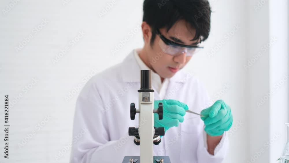 Asian scientist or researcher man use forceps to pick up plant tissue on glass slide then analysis by microscope in biology laboratory or classroom then record the data to study with biotechnology. Asian scientist or researcher man use forceps to pick up plant tissue on glass slide then analysis by microscope in biology laboratory or classroom then record the data to study with biotechnology.
