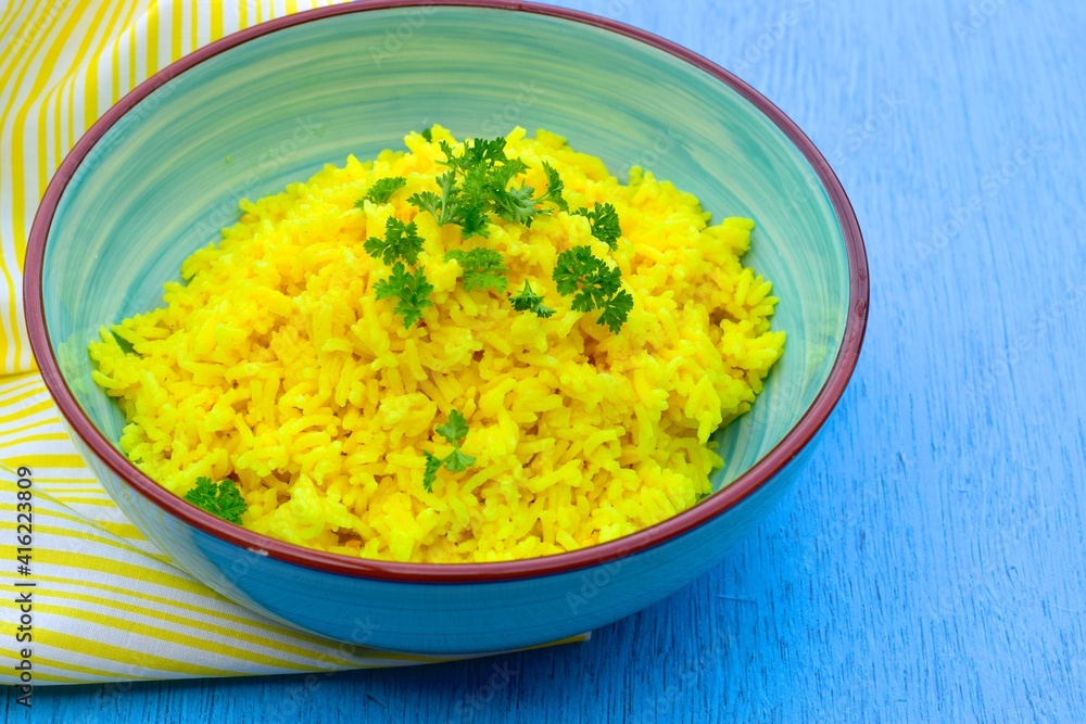 Indonesian yellow turmeric rice or Nasi Kuning in a bowl garnish with chopped parsley. Blue background