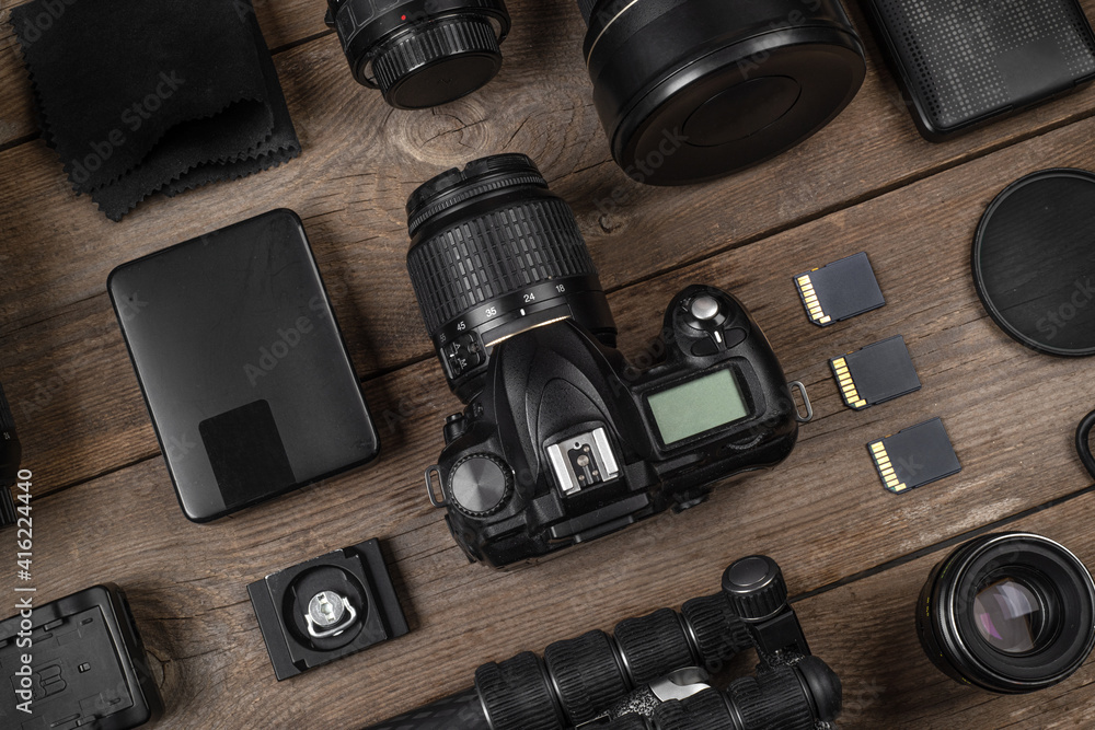 A set of camera and photographic equipment (lens, tripod, filter, memory card, hard disk) on a wood table. Professional photographer accessories background. - obrazy, fototapety, plakaty 