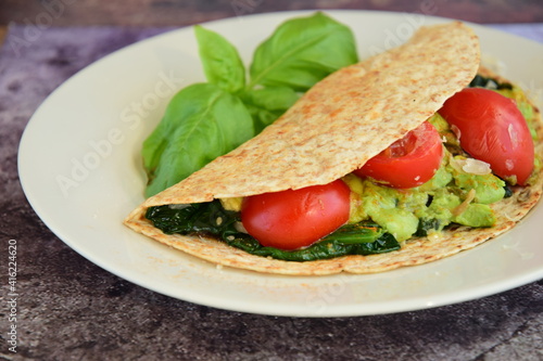 Whole wheat tortilla wrap filled with avocado, spinach and tomato garnish with basil leaf
