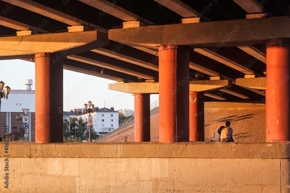 A couple in love is sitting under a car bridge between huge columns, in the light of the setting sun on a summer evening A couple in love is sitting under a car bridge between huge columns, in the light of the setting sun on a summer evening