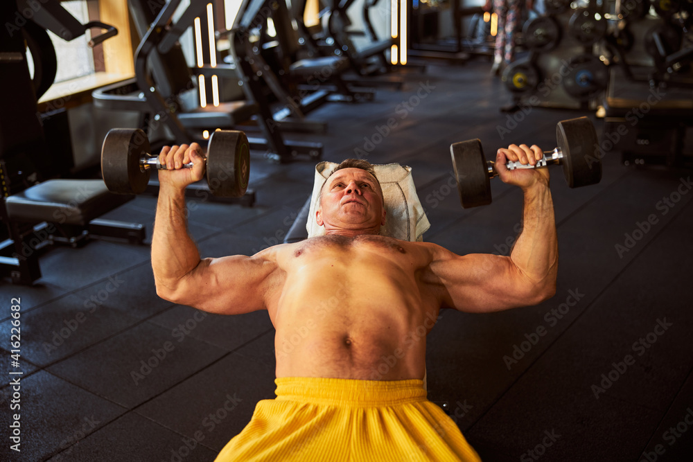 Fototapeta premium Committed muscular man doing exercises with dumbbells