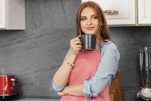 Young woman drinks tea while standing in kitchen