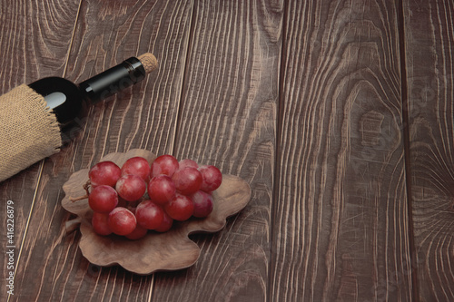 A bottle of expensive wine with grapes on a plate made of black walnut wood lie on the background of old boards