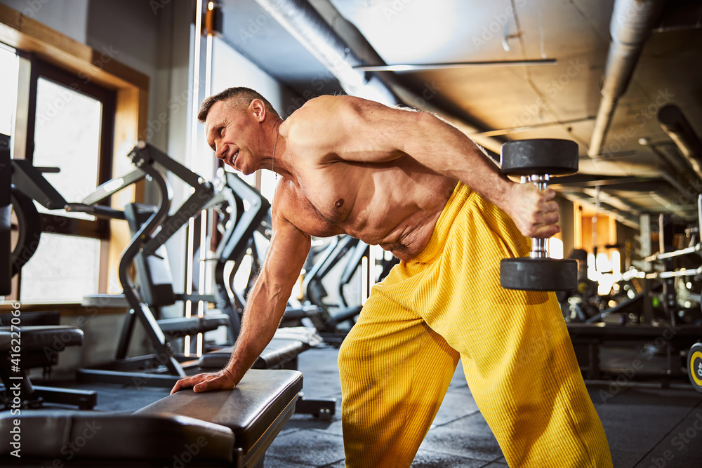 Naklejka premium Mature bodybuilder exercising with set of dumbbells