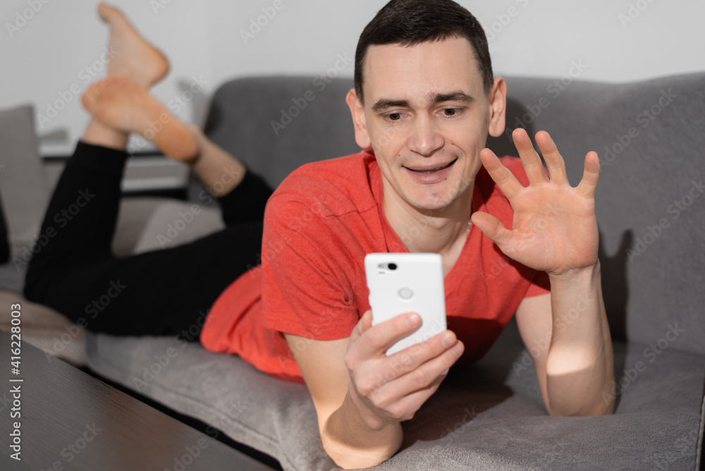 A young man relaxing at home on a sofa chatting on his mobile with a smile A young man relaxing at home on a sofa chatting on his mobile with a smile