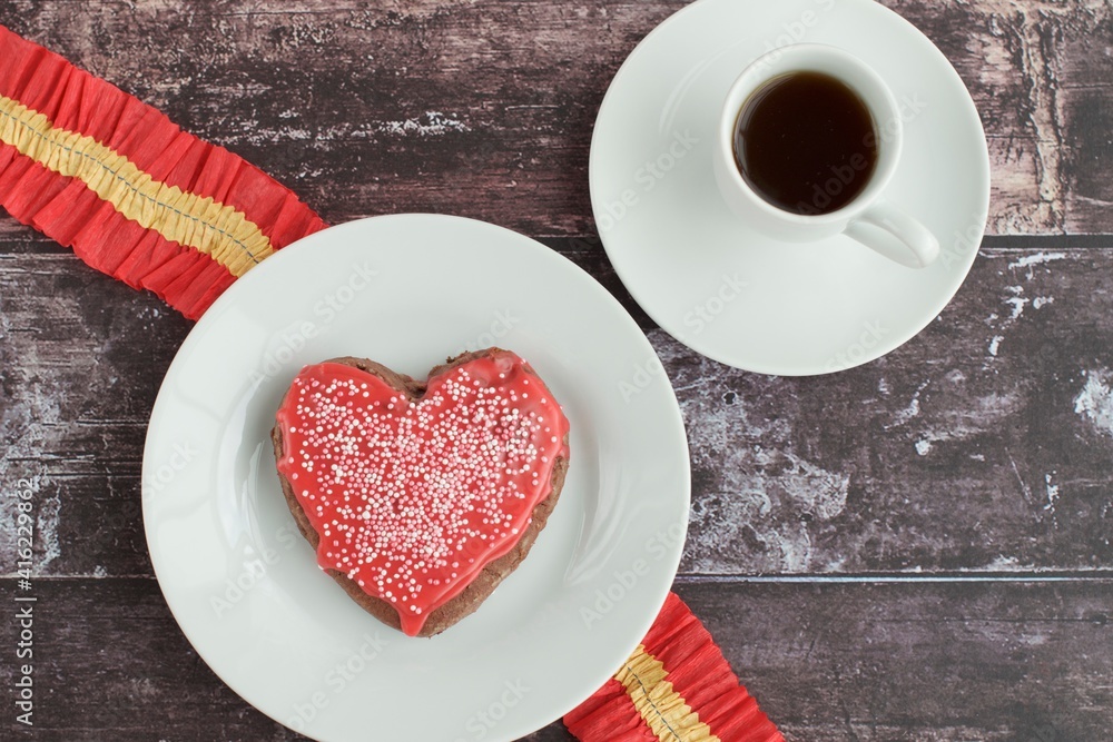 Heart shaped Valentine's cookie with red sugar glaze and sprinkles, served with coffee. Flat lay