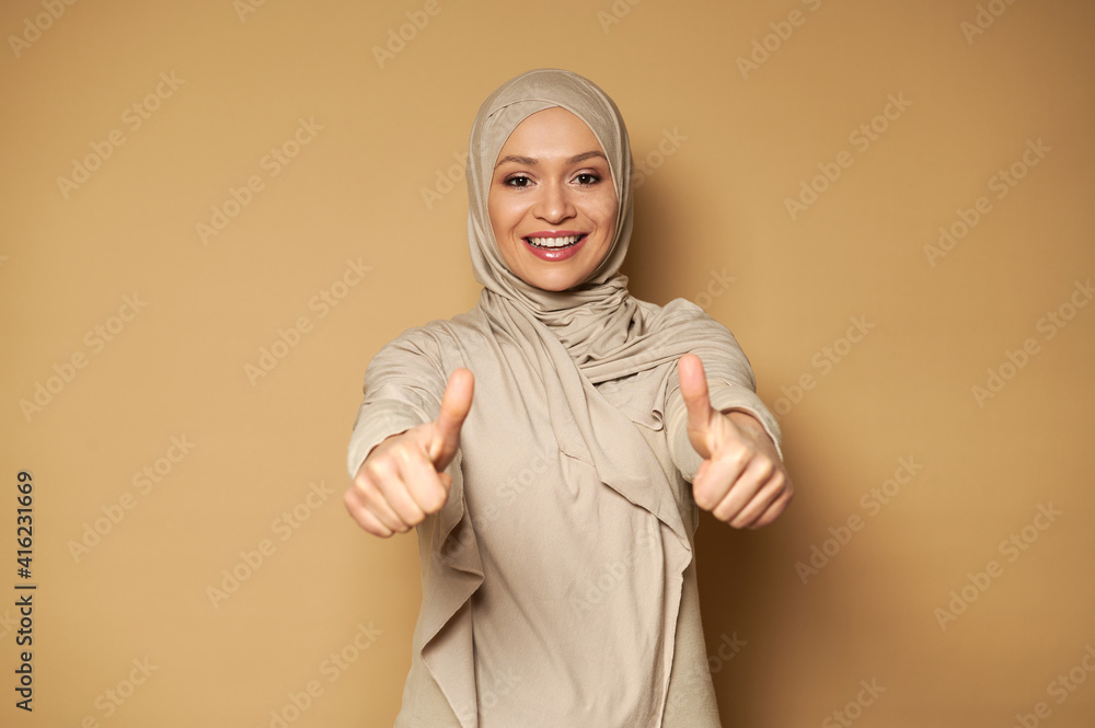 Fototapeta premium Beautiful Muslim woman in hijab cute smiling with toothy smile and showing thumbs up while looking to the camera