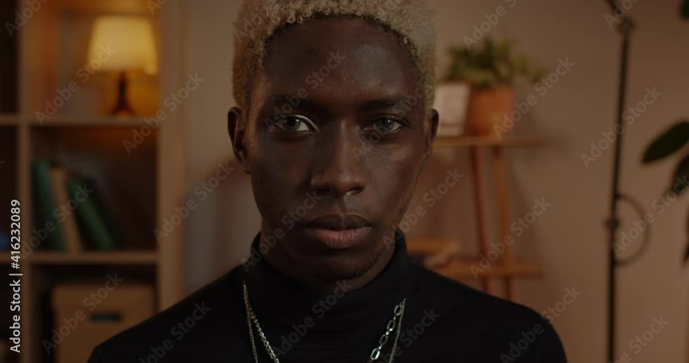 Crop view of handsome young man looking to camera. Portrait of stylish millennial male person with dyed hair posing while sitting at home in evening Crop view of handsome young man looking to camera. Portrait of stylish millennial male person with dyed hair posing while sitting at home in evening