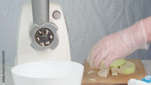 Grinding cabbage in an electric meat grinder for making lazy cabbage rolls. The chef's hand in a glove turns on the meat grinder and puts cabbage into it.
