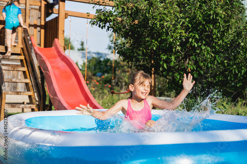 Staycation at home. Little girl in swimsuit rolls down slide into inflatable rubber pool. Swim activity in backyard of country house. Summer,relaxation on isolation,quarantine of coronavirus covid-19