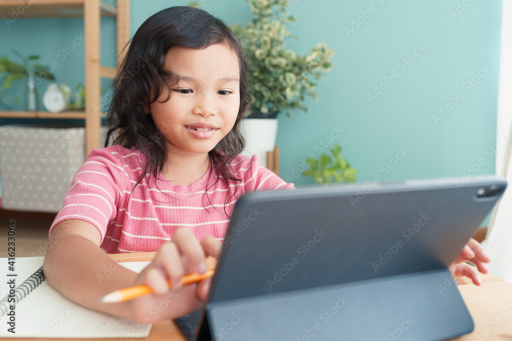 Asian little girl learning online with a tutor via internet on tablet at home Asian little girl learning online with a tutor via internet on tablet at home