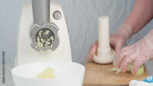 Grinding onions in an electric meat grinder to add to the minced meat. The gloved hand of the cook turns on the meat grinder and puts the onion into it.