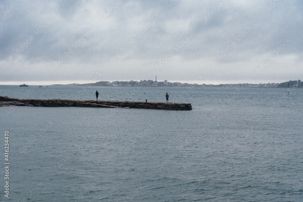 Back view of two adults standing on pier facing to the calm sea against the Island of Batz, freedom concept. Roscoff, Brittany