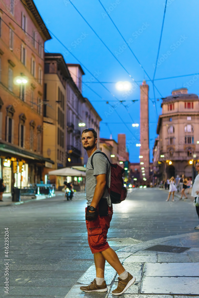 Tourist man with backpack walk on the night summer street in Italy. Vertical photo. Bologna Tourist man with backpack walk on the night summer street in Italy. Vertical photo. Bologna