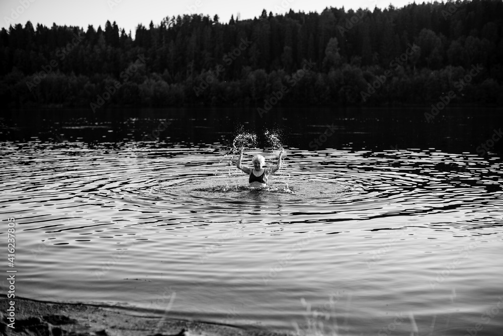 Obraz premium An old woman in the summer river at sunset. Black and white photo.