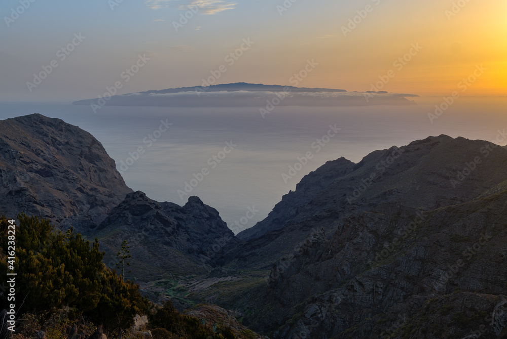 View from Tenerife's Teno Mountains to the remote island of La Gomera. It's just before sunrise. Behind the valley is the Atlantic Ocean. There are some clouds in front of the island.