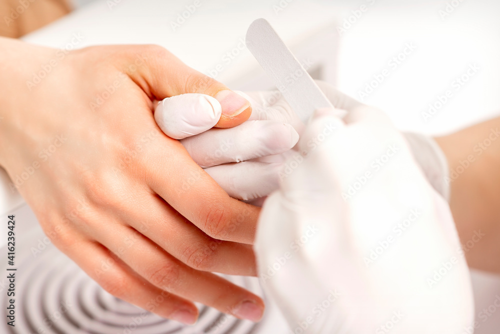 Manicure master wears white gloves with nail file doing manicure on female fingernails in a nail salon Manicure master wears white gloves with nail file doing manicure on female fingernails in a nail salon