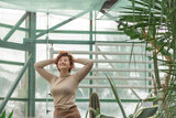 A beautiful plus size girl enjoying standing among the green plants of the greenhouse. Cottagecore style 
