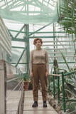 A beautiful plus size girl standing among the green plants of the greenhouse. Cottagecore style 