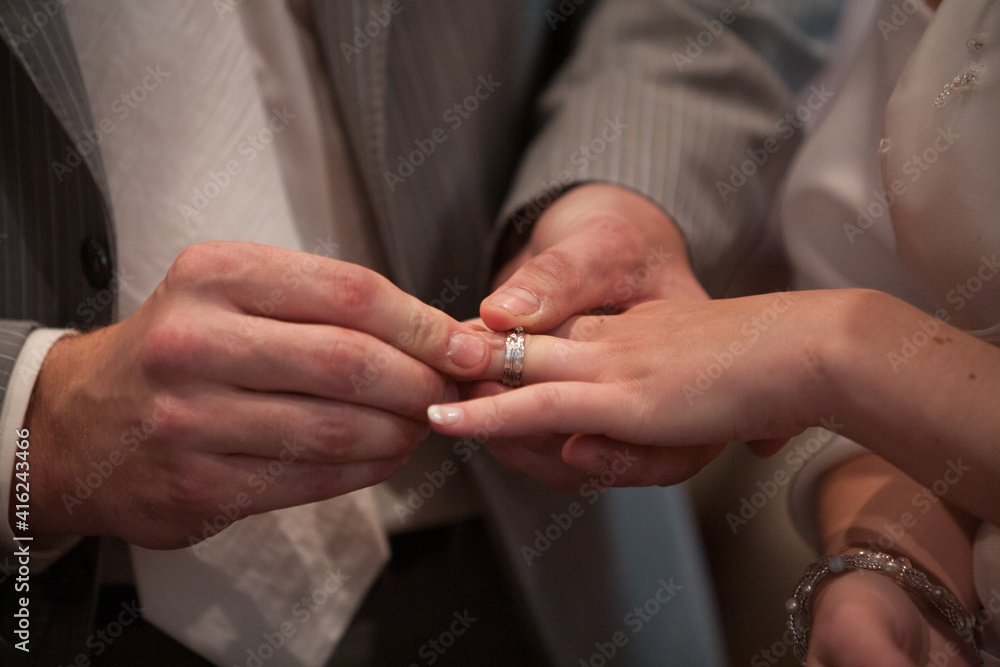 Closeup of bride putting a wedding ring onto the groom's finger. Couple exchanging wedding rings. High quality photo