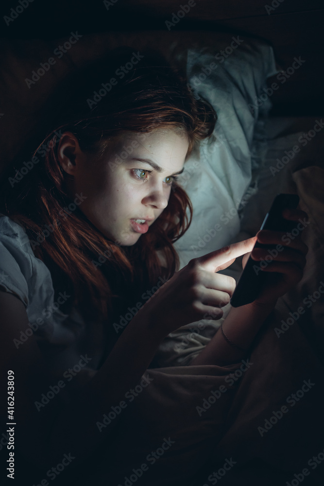 smiling woman with a phone in her hands at night lies in bed lifestyle communication