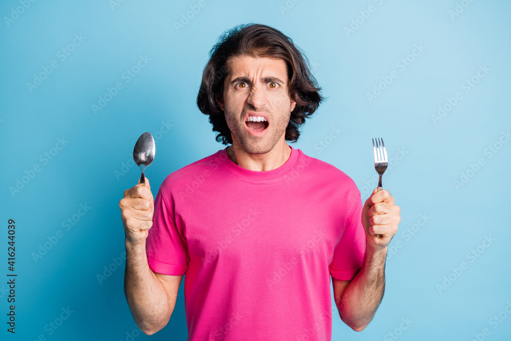 Portrait of outraged mad irritated guy holding in hands fork spoon vegan food reaction isolated over bright blue color background Portrait of outraged mad irritated guy holding in hands fork spoon vegan food reaction isolated over bright blue color background