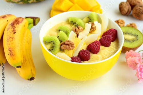 Mango banana pineapple smoothie bowl topped with raspberry, kiwi, walnut and coconut chips