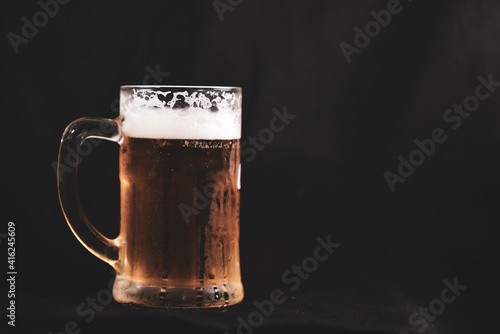 a pint full of beer and foam on a black background. alcoholic soft drink