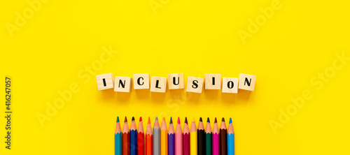 Inclusion banner word on wooden cubes and pencils on yellow background